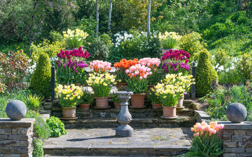 Barocke Gartenanlage mit Gartendekoration – Klassische Sonnenuhr auf Steinstockel & Blumen im Pflanzgefäß