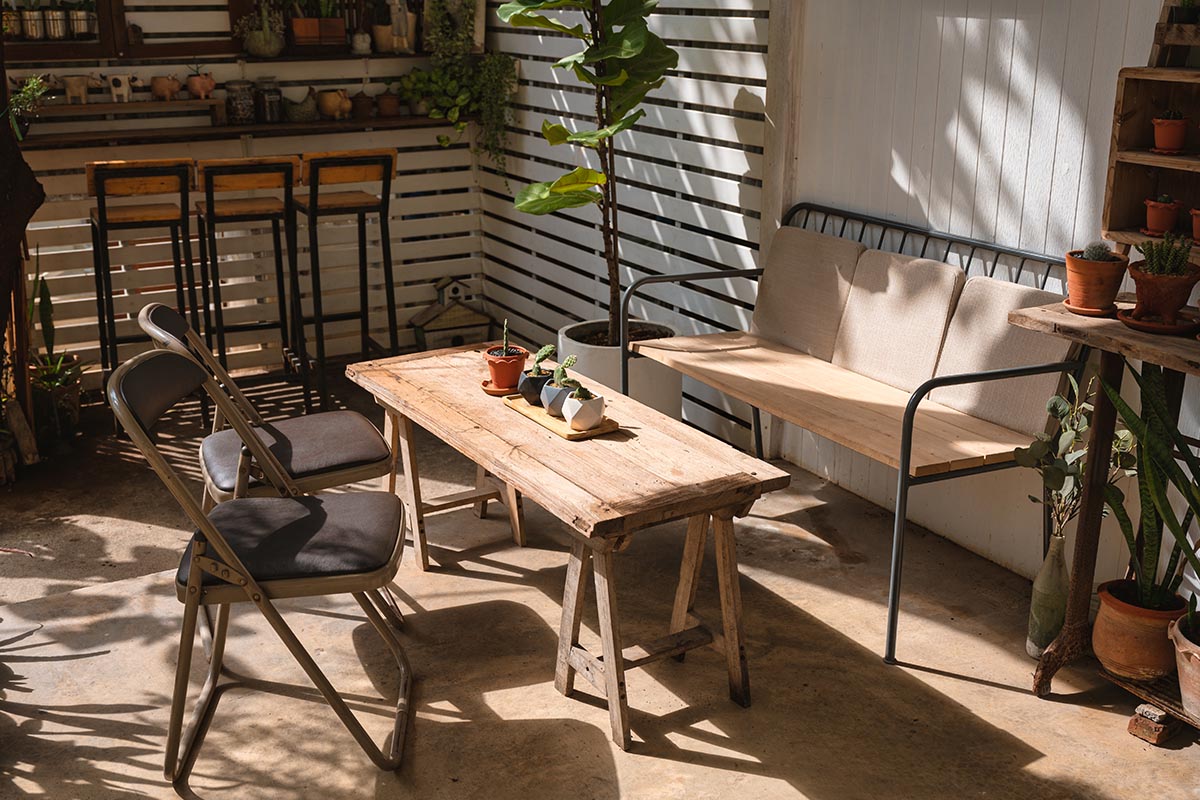 Rustikal gestaltete Terrasse mit Bank, Stühlen und einfachen Holztisch im Landhausstil.