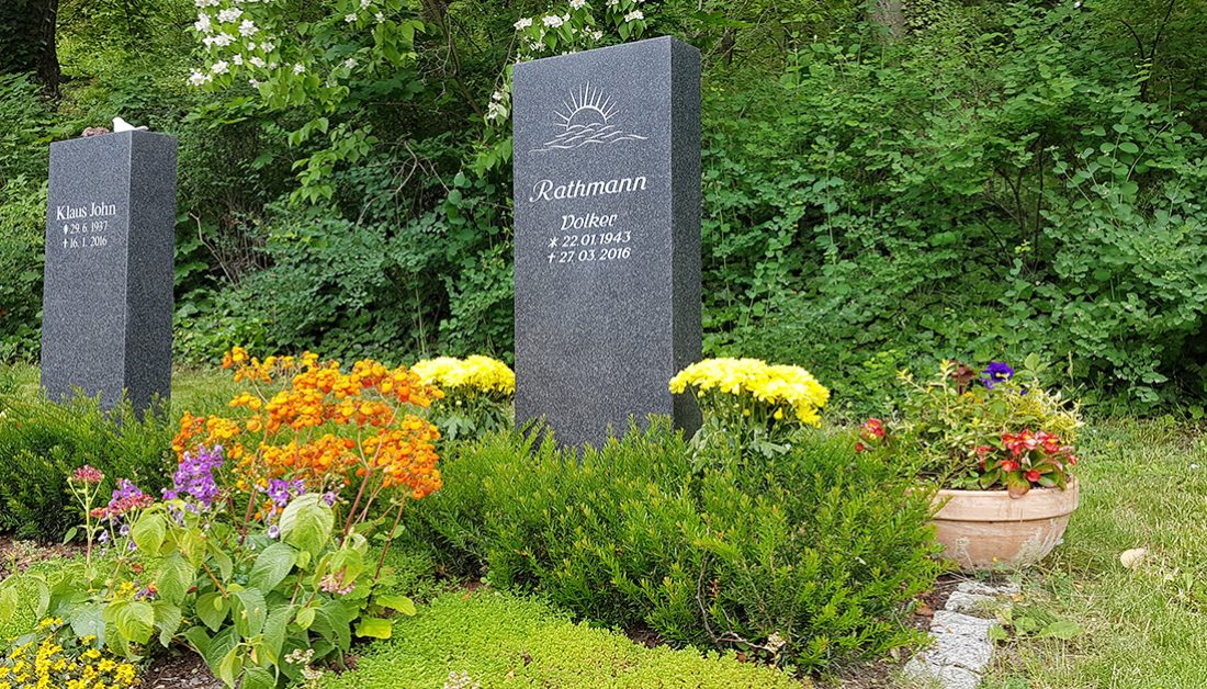 Moderne Grabgestaltung eines Doppelgrabes mit dunkler Granitstele – natürliche Grabeinfassung mit Eibe & Bepflanzung mit einer Mischung aus Bodendeckern und Sommerblumen