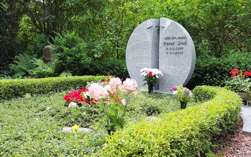 Runder zeiteiliger Doppelgrabstein aus Granit – moderne Grabgestaltung mit immergrünen Pflanzen & natürlicher Grabeinfassung mit Buchsbaum