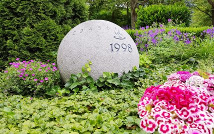 Moderne Urnengrabstätte mit Grabstein als Kugel – ganzjährige Grabbepflanzung pflegele...