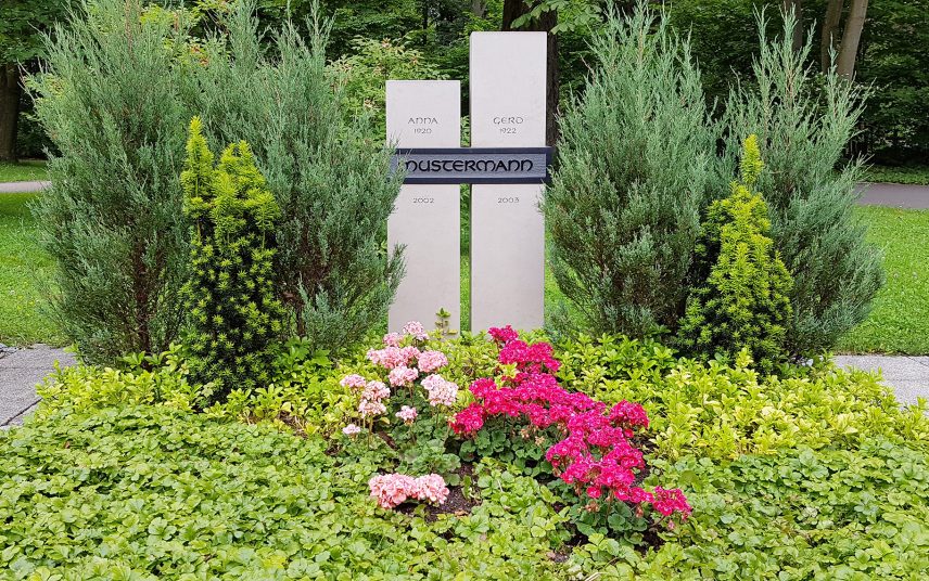 Zweiteiliger Doppelgrabstein aus Kalkstein mit einer modernen Grabbepflanzung aus Bodendeckern  immergrünen Nadelgehölzen und Sommerblumen