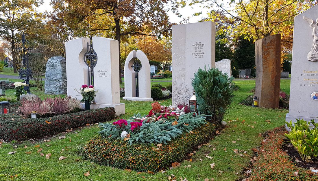 Moderne Grabgestaltung zu Allerheiligen eines Einzelgrabes mit Reisig und Grabgesteck - Grabstein aus Kalkstein mit Bodendecker als Einfassung