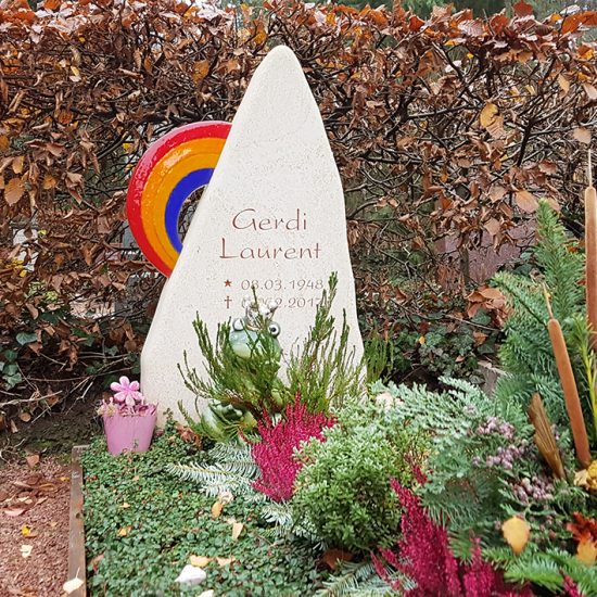 Modernes Einzelgrab mit Grabstein aus Kalkstein und Regenbogen aus Glas - pflegeleichte Grabgestaltung zu Allerheiligen mit Grabgesteck und Herbstbepflanzung
