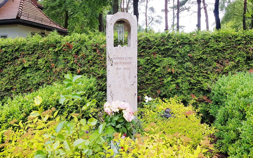 Moderne Grabstele aus Kalkstein mit Windspiel für ein Einzelgrab – ganzjährige Grabbepflanzung mit Buchsbaum & Blühstauden