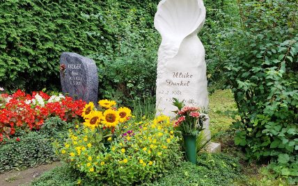 Heller Einzelgrabstein aus Kalkstein mit einer stilisierten Muschel & schöner Grabbepflan...