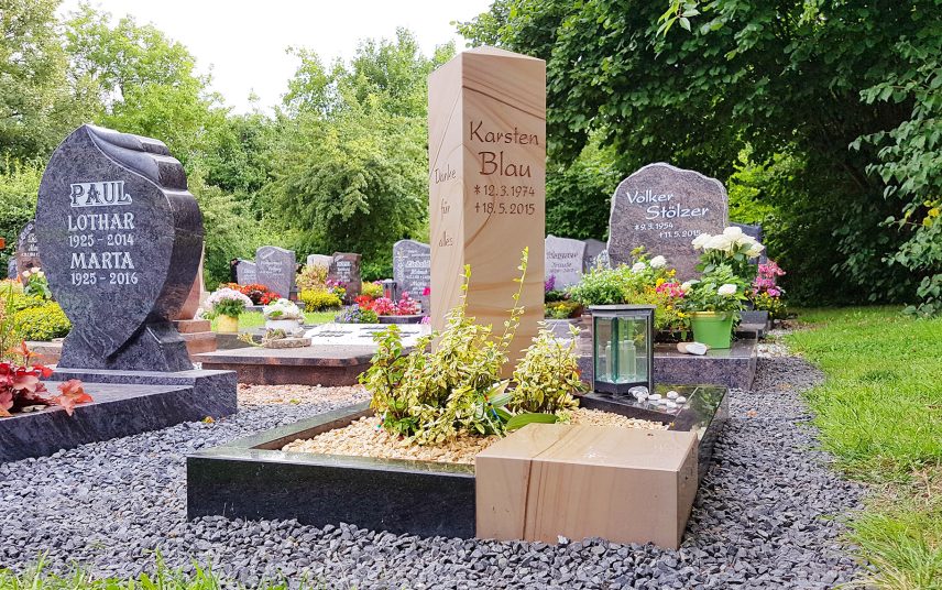Modernes Urnengrab mit Stele aus Sandstein poliert und einer Einfassung aus Granit & Sandstein – pflegeleichte Grabgestaltung mit Kies und Bodendeckern