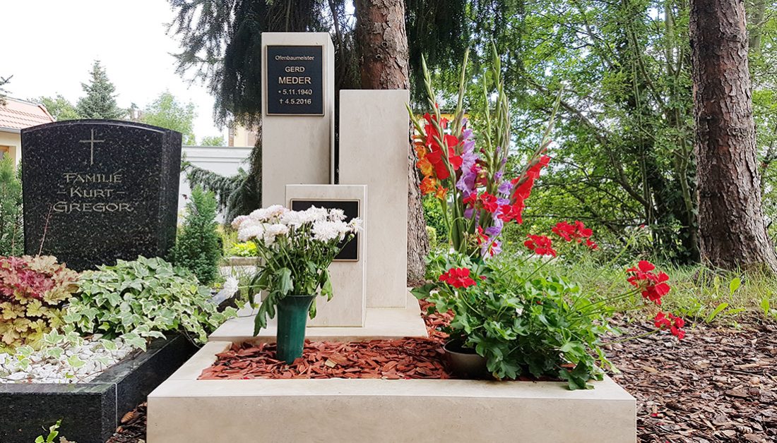Modern gestaltetes Urnengrab mit Grabstelen und Grabeinfassung aus hellem Kalkstein & Bronzeplatten - pflegeleichte Grabgestaltung mit Rindenmulch und Blumen