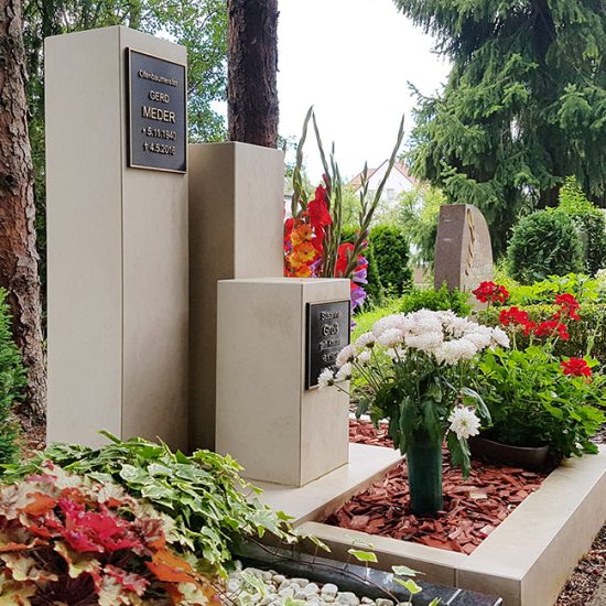 Modern gestaltetes Urnengrab mit Grabstelen und Grabeinfassung aus hellem Kalkstein & Bronzeplatten - pflegeleichte Grabgestaltung mit Rindenmulch und Blumen