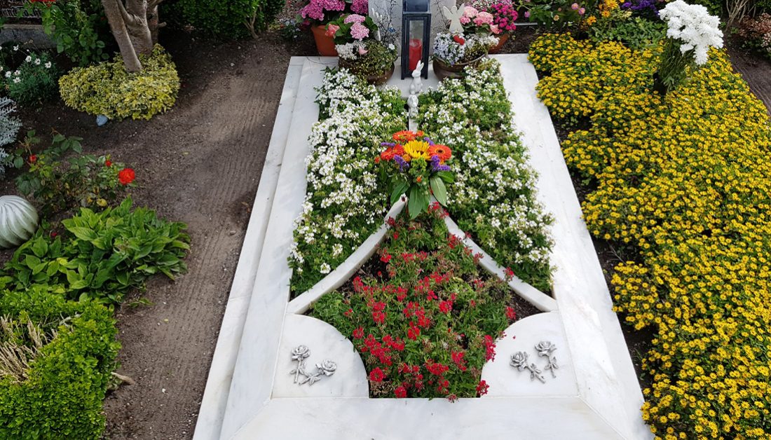 Moderner Einzelgrabstein mit aufwendig gestalteter Grabumfassung aus weißem Marmor - prachtvolle Bepflanzung für den Sommer mit blühenden Grabpflanzen