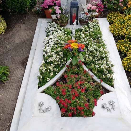 Moderner Einzelgrabstein mit aufwendig gestalteter Grabumfassung aus weißem Marmor - prachtvolle Bepflanzung für den Sommer mit blühenden Grabpflanzen