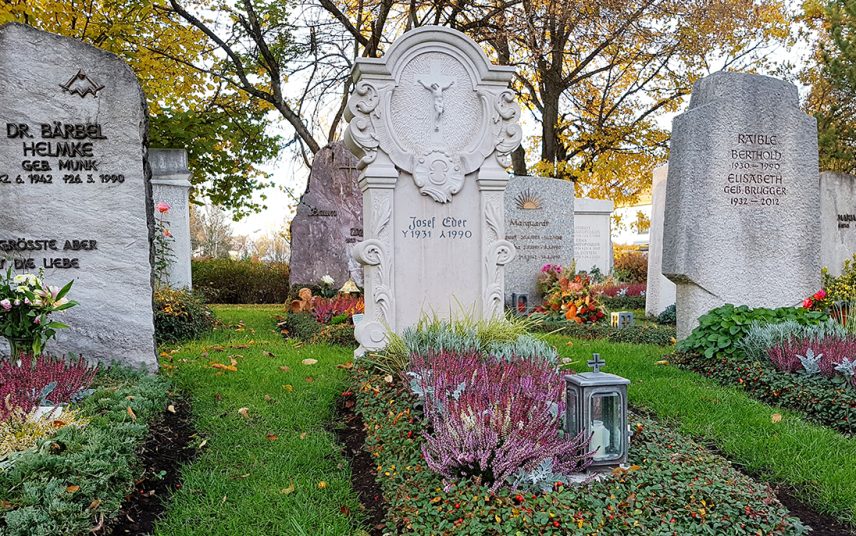 Klassisches Einzelgrab mit aufwendig verziertem Grabstein mit christlichem Motiv – pflegeleichte Grabbepflanzung mit Blumen & immergrünen Bodendeckern