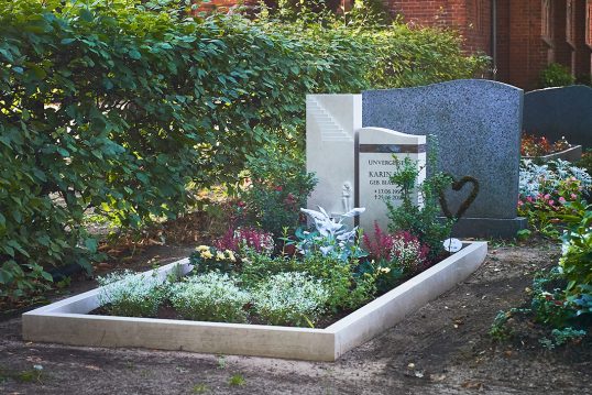 Idee für die Grabgestaltung – Gepflegtes Doppelgrab aus Kalkstein & Bronzeornament – pflegleichte Grabbepflanzung mit Stauden und Gehölzen