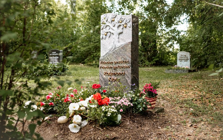 Romantisches Granitgrabmal mit Baum & vergoldeten Früchten – sommerlicher Blumenschmuck umrahmt den Grabstein