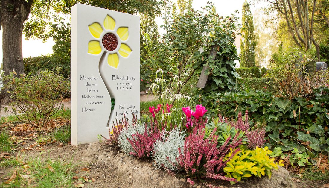 Idee für die Grabgestaltung - Einzelgrabstein aus hellem Kalkstein mit Blume als Glasornament - schöne sommerliche Grabbepflanzung
