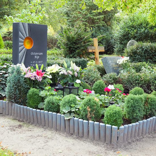 Moderne Einzelgrabanlage aus dunklem Granit & Glas - eine pflegeleichte Grabbepflanzung ziert das Grab