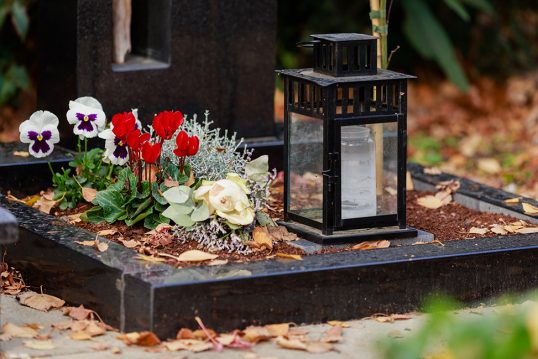 Urnengrab Beispielgestaltung –  Moderner Granitgrabstein mit Öffnung und Olivenholzzweig & Grabeinfassung – Schlichter Grabschmuck