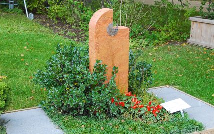 Modern gestalteter Grabstein aus rotem Travertin- halbrund mit kleinem Bronzerelief – Gr...