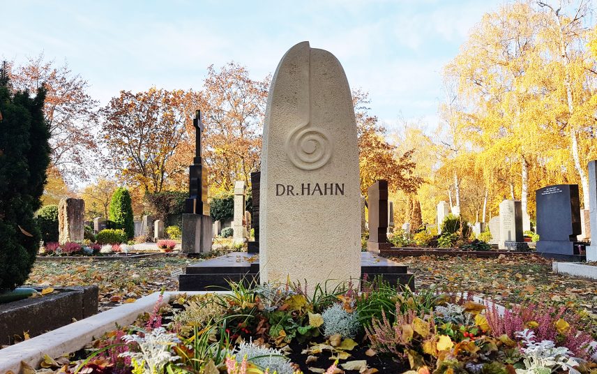Moderner Doppelgrabstein aus schwarzem poliertem Granit mit Öffnung und zwei Bronzeengeln – Üppige Grabgestaltung mit Frühlingsblumen und Grabdekoration