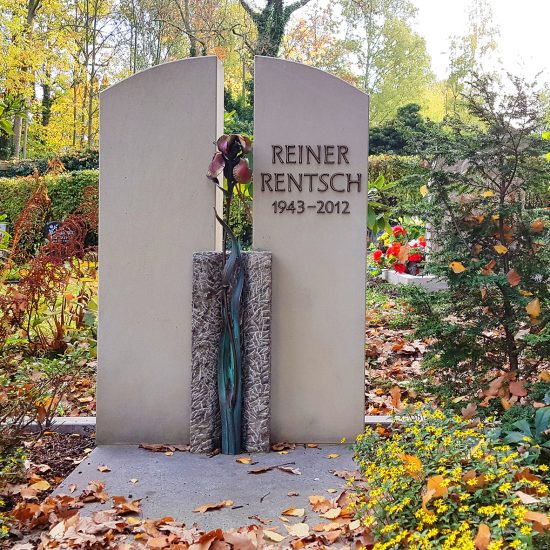 Doppelgrab mit geteiltem Grabstein aus Kalkstein  Einfassung  Trittplatte & Bronzefigur / Grabbepflanzung mit Nadelgehölzen und gelben Sommerblumen