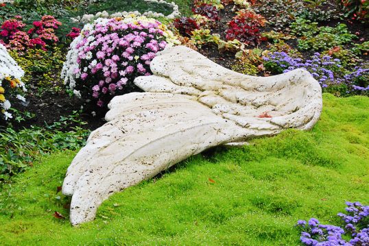 liegender Grabstein aus Travertin – Engelsflügel – freie Grabgestaltung mit Bärenfellgras und bunten Herbstblumen