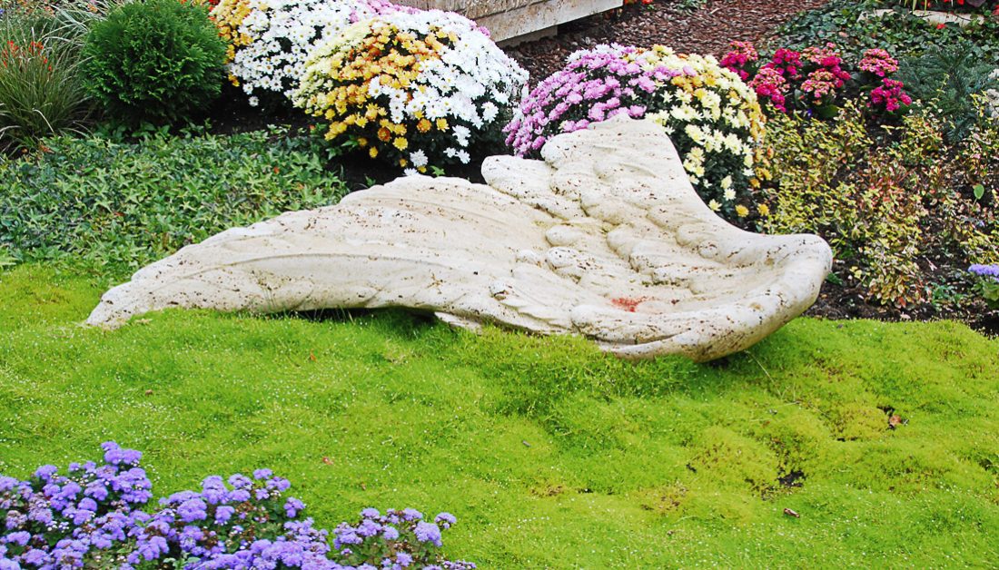 liegender Grabstein aus Travertin – Engelsflügel – freie Grabgestaltung mit Bärenfellgras und bunten Herbstblumen