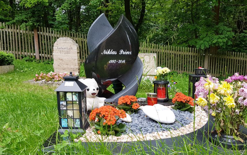 Moderner Grabstein für ein Kindergrab aus schwarzem Granit als Spirale gedreht mit Einfassung –  Grabgestaltung mit Kies und Grabschmuck