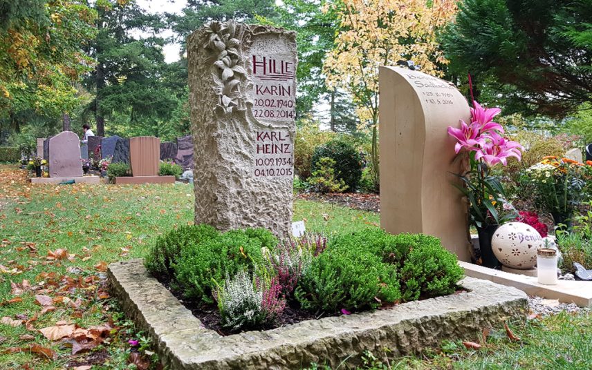 verzierte Stele und Einfassung aus Kalkstein mit Blütenornamenten für ein Urnengrab – herbstliche Grabbepflanzung