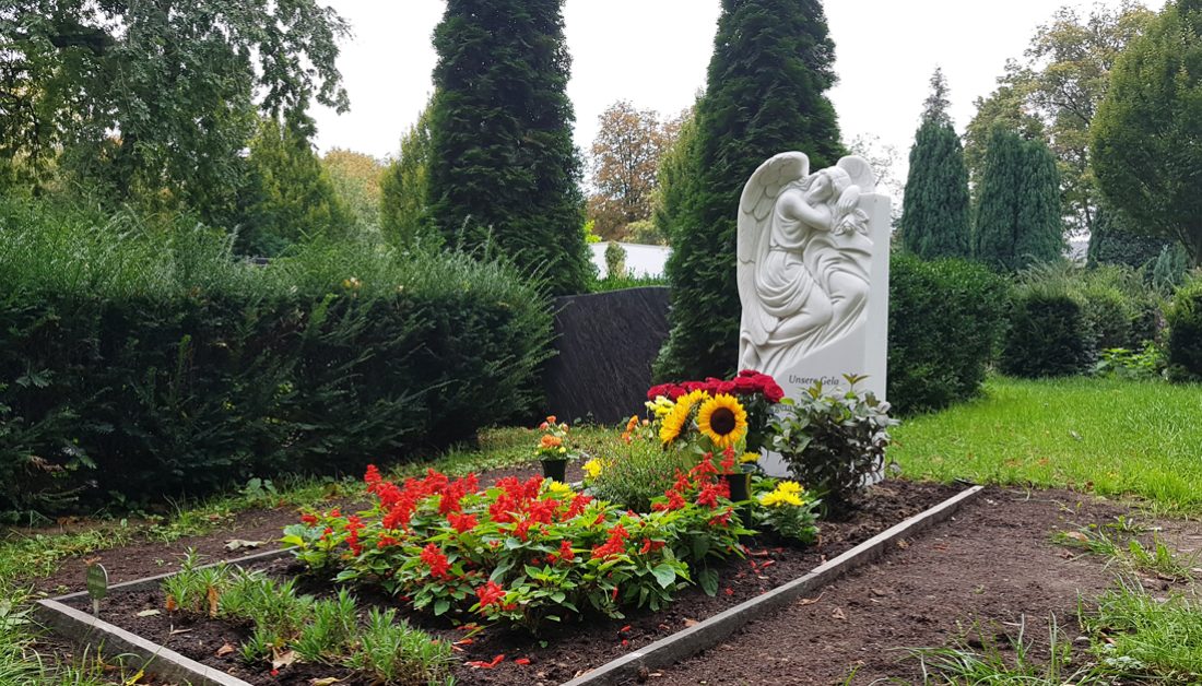 Klassisches Grabmal mit Engel aus Marmor für ein Einzelgrab / Grabgestaltung mit Blumensträußen und blühenden Stauden