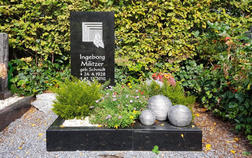 Kleines modernes Urnengrab aus schwarzem Granit- gestaltet mit einer Sommerbepflanzung  Kies und Garbdekoration