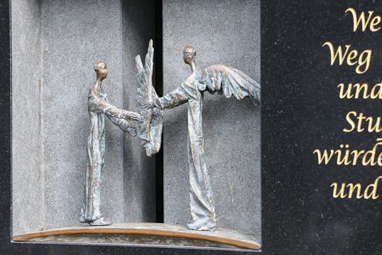 Moderner Doppelgrabstein aus schwarzem poliertem Granit mit Öffnung und zwei Bronzeengeln – Üppige Grabgestaltung mit Frühlingsblumen und Grabdekoration