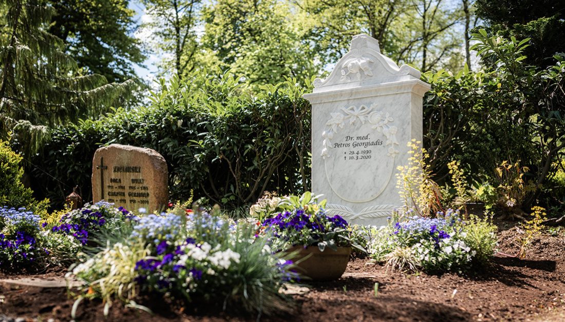 Klassischer Doppelgrabstein aus weißem Marmor mit floralen Details - Gestaltung der Grabstätte mit Frühjahrsbepflanzung
