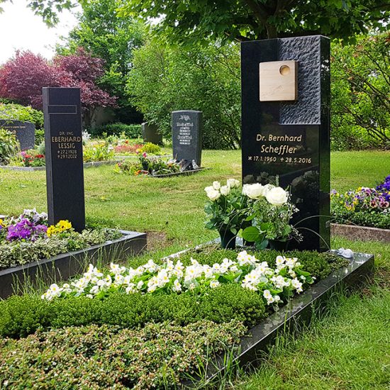 Moderner Grabstein aus schwarzem Granit mit unterschiedlicher Oberflächenbearbeitung und Buntsandsteineinleger mit Vergoldung - professionelle Grabbepflanzung durch einen Friedhofsgärtner