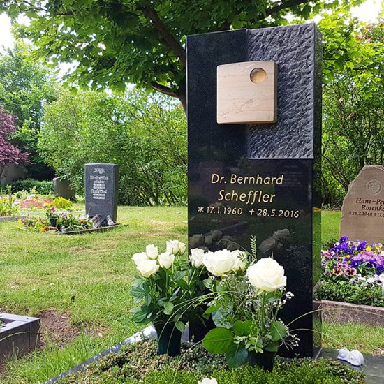 Moderner Grabstein aus schwarzem Granit mit unterschiedlicher Oberflächenbearbeitung und Buntsandsteineinleger mit Vergoldung - professionelle Grabbepflanzung durch einen Friedhofsgärtner