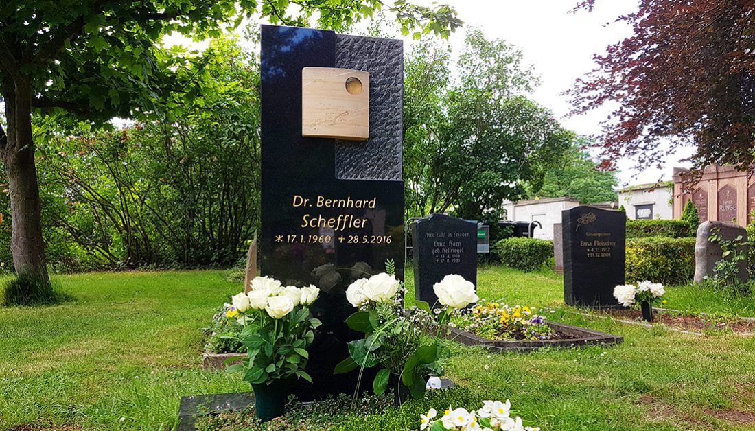 Moderner Grabstein aus schwarzem Granit mit unterschiedlicher Oberflächenbearbeitung und Buntsandsteineinleger mit Vergoldung – professionelle Grabbepflanzung durch einen Friedhofsgärtner