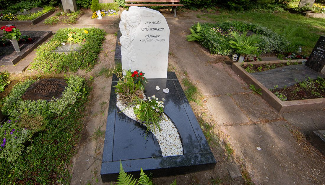 Schönes Urnengrab im Kontrast Schwarz/ Weiß aus einem Marmorgrabstein und einer Graniteinfassung/ Grabgestaltung mit Abdeckplatte  Kies & Blumengesteck