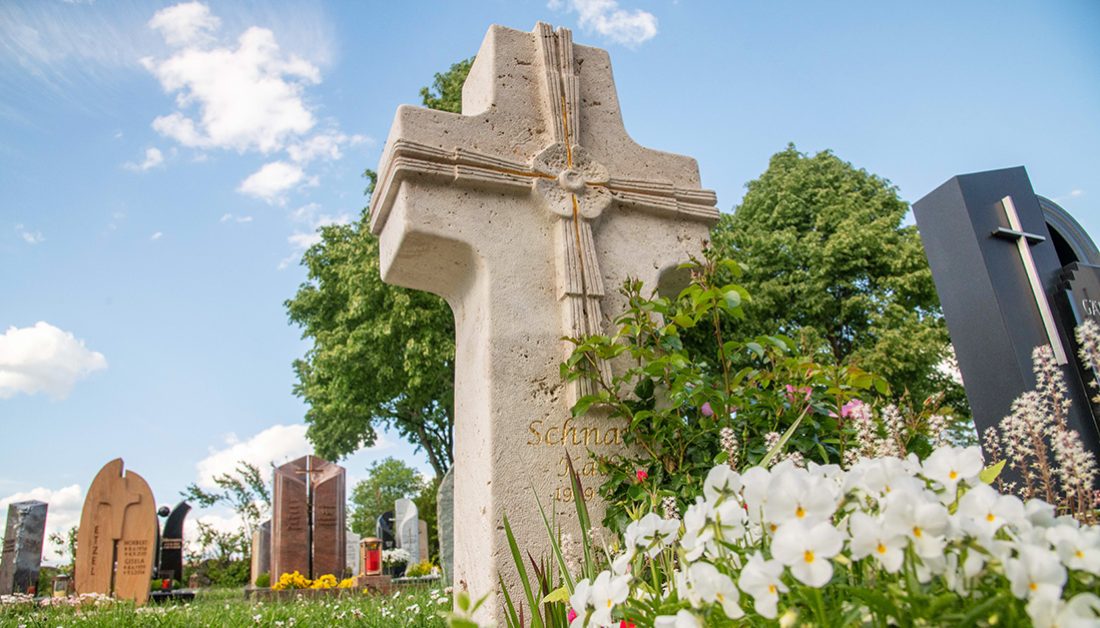 Klassischer Einzelgrabstein als Steinkreuz aus hellem Kalkstein mit Vergoldungen - Grabgestaltung mit mehrjährigen Pflanzen und kleinen Gehölzen