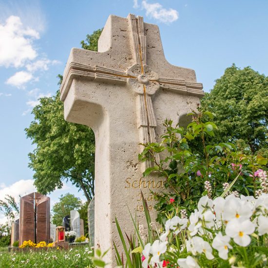 Klassischer Einzelgrabstein als Steinkreuz aus hellem Kalkstein mit Vergoldungen - Grabgestaltung mit mehrjährigen Pflanzen und kleinen Gehölzen