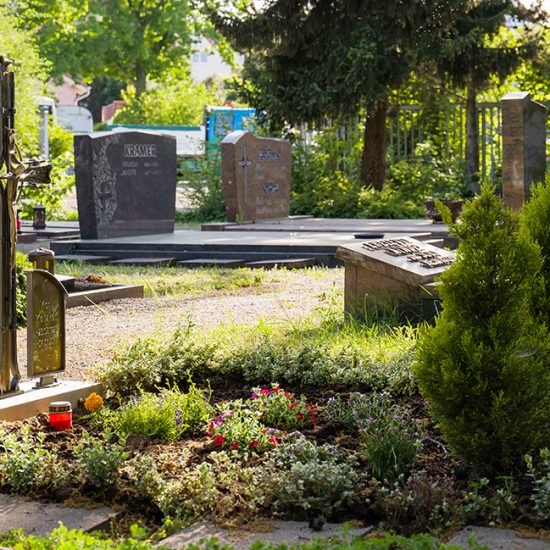 Klassische Doppelgrabanlage mit einem schmiedeeisernen Grabkreuz und Bronzetafeln - Grabgestaltung mit Solitärgehölzen und Bodendeckern