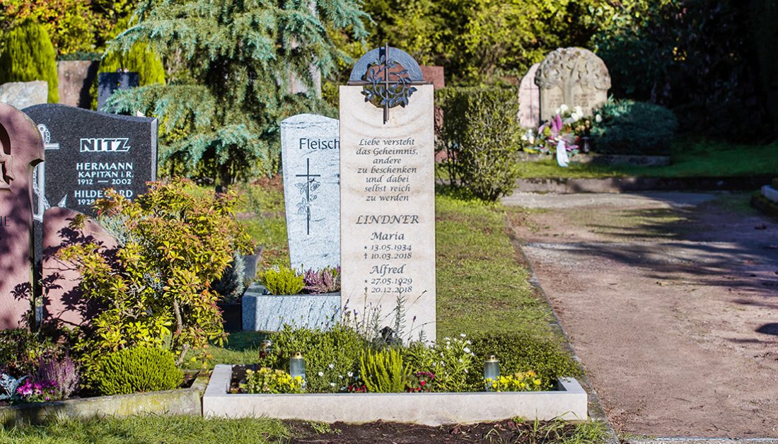 modernes Urnengrab – Idee zur Gestaltung mit einem Grabstein aus hellem Kalkstein und einem runden Bronzerelief mit christlichem Symbol