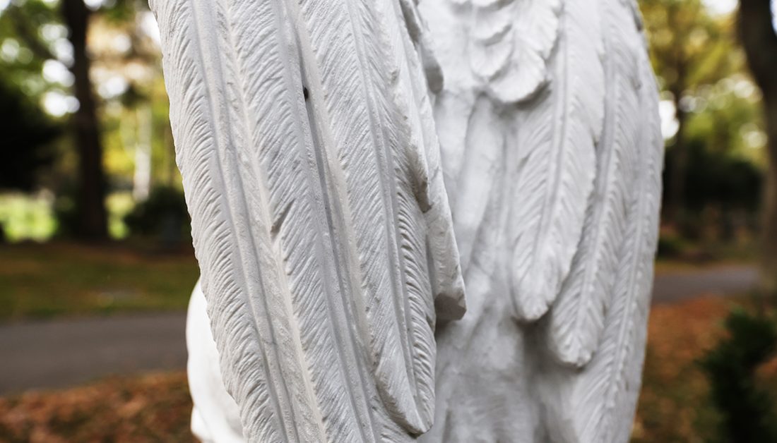 Klassische Grabstele mit knieendem Marmorengel auf einem Sockel – pflegeleichte Grabbepflanzung mit Solitärgehölzen und einer Einfassung aus winterharten Stauden