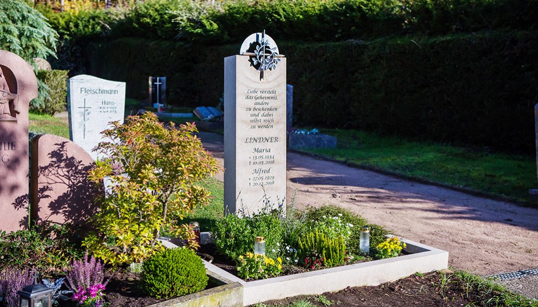 modernes Urnengrab – Idee zur Gestaltung mit einem Grabstein aus hellem Kalkstein und einem runden Bronzerelief mit christlichem Symbol