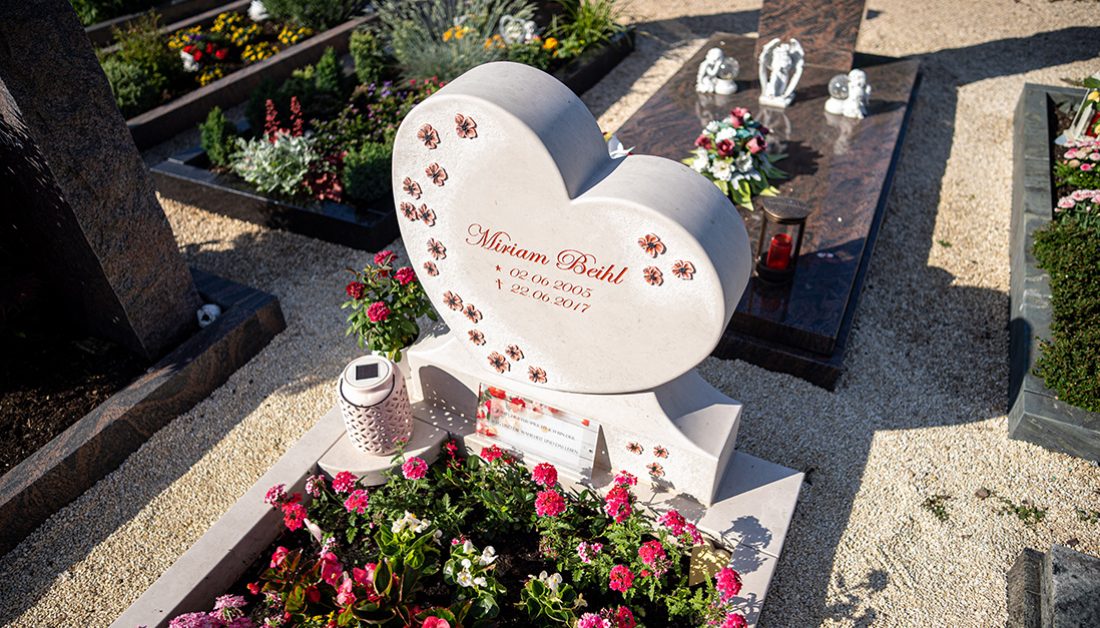 Einzelgrabmal in Herzform aus hellem Kalkstein mit Sockel  Einfassung und Grablaterne - sommerliche Grabbepflanzung mit Blumen