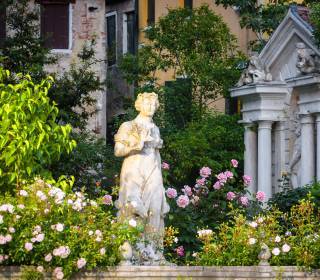 antike Skulptur für den Garten weiblich zwischen Rosensträuchern