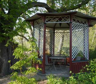 kleiner Gartenpavillon Achteck antik aus Holz als Sitzplatzüberdachung unter einem alten Baum