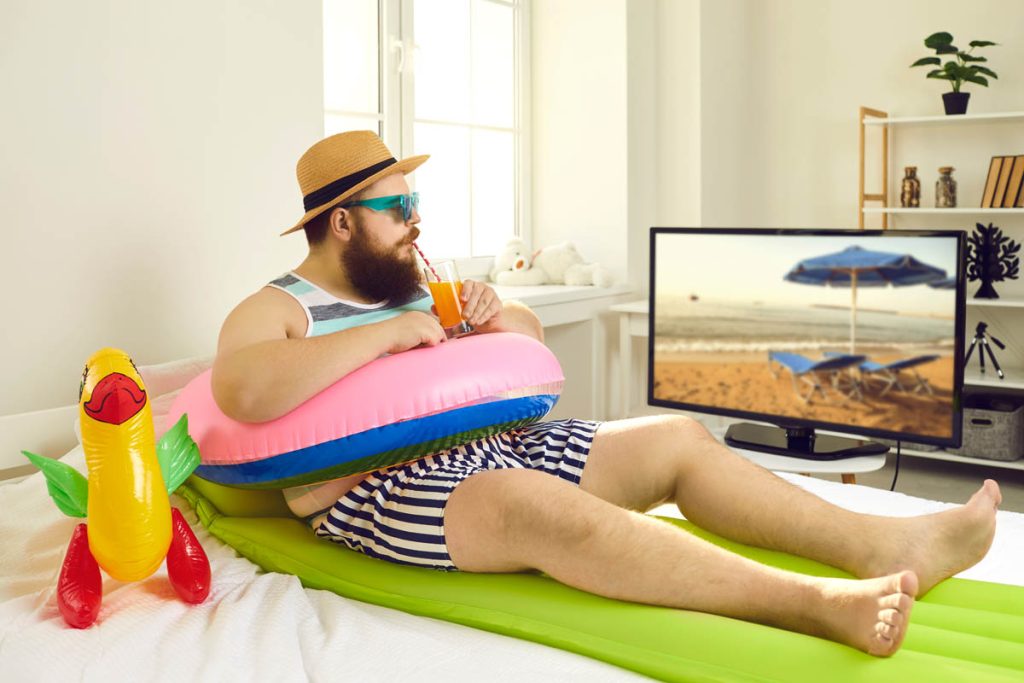 Lustiges Bild - Mann sitzt zu Hause vor dem Fernseher mit Urlaubsfeeling