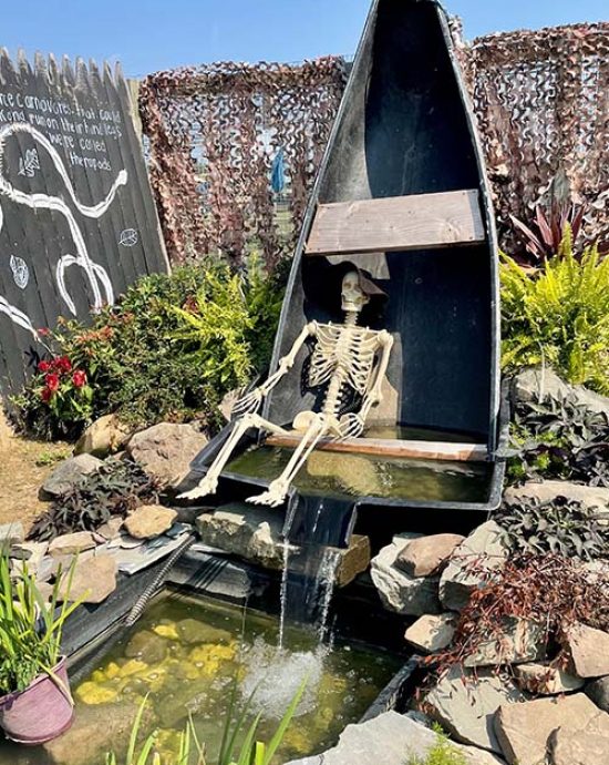 Lustige Gartendekoration am Gartenteich mit Skelett und Boot