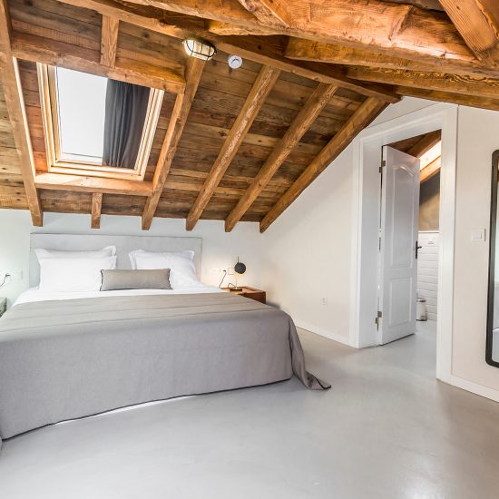 Wohnidee - Gemütliches Landhaus-Schlafzimmer im Dachgeschoß eines Chalets - freigelegte Holzbalkendecke & Doppelbett mit Nachtkästchen