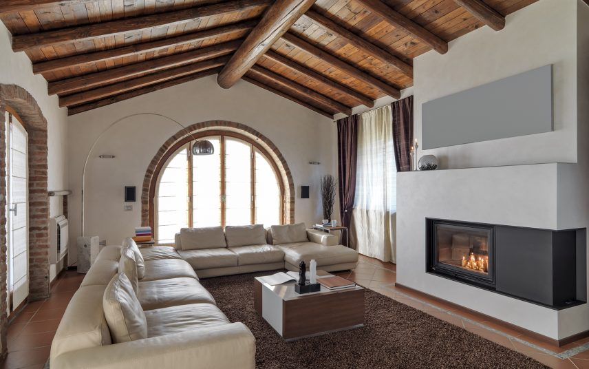 Gemütliches Ferienhaus Idee – mediterraner Stil – Wohnen unterm Dach/ Leder-Eckcouch vor einem Kamin & rustikale Holzdeckenbalken