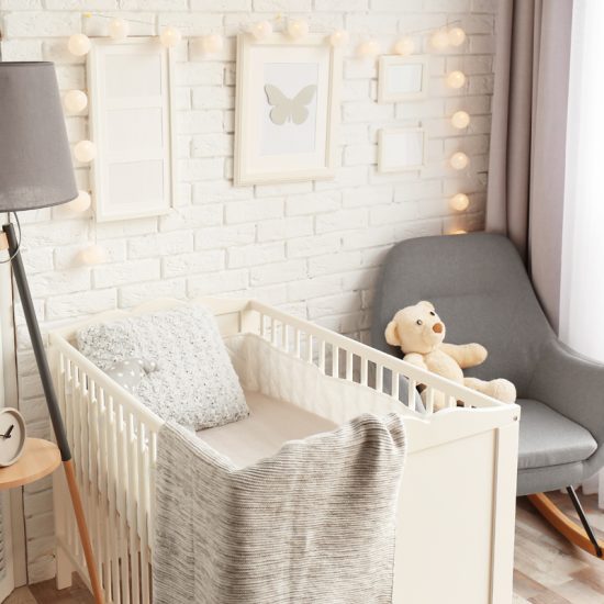 Landhaus Babyzimmer in weiß Gestaltungsidee - Mädchenzimmer mit weißen Babybettchen & Tripodlampe mit grauem Lampenschirm - grauer Schaukelstuhl - Wandgestaltung mit weißen Bilderrahmen & Lichterkette
